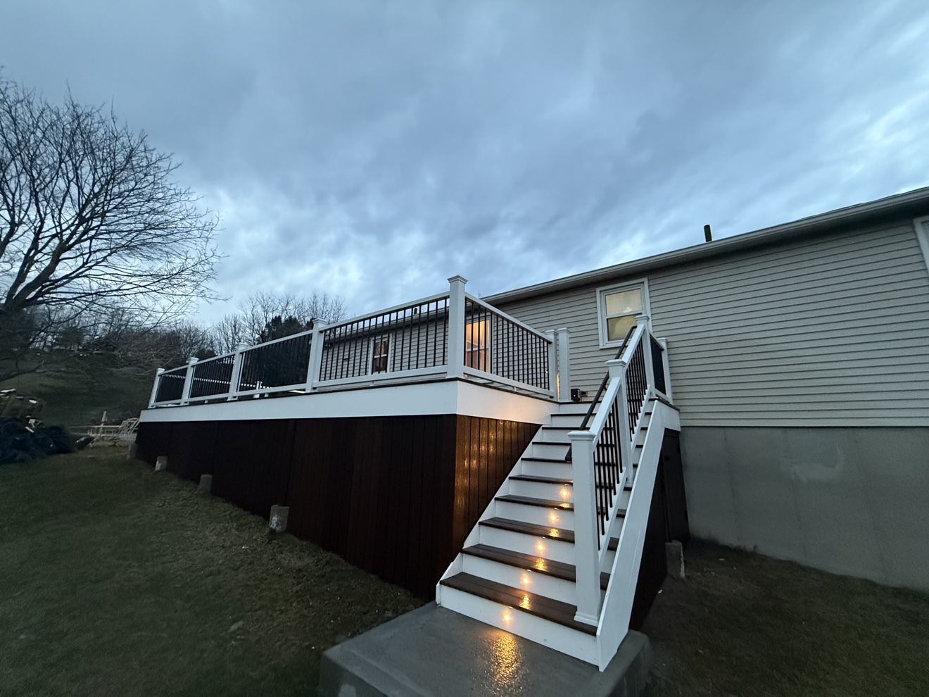 Raised composite deck built by E.B.R Deck Builder, with an illuminated staircase at dusk