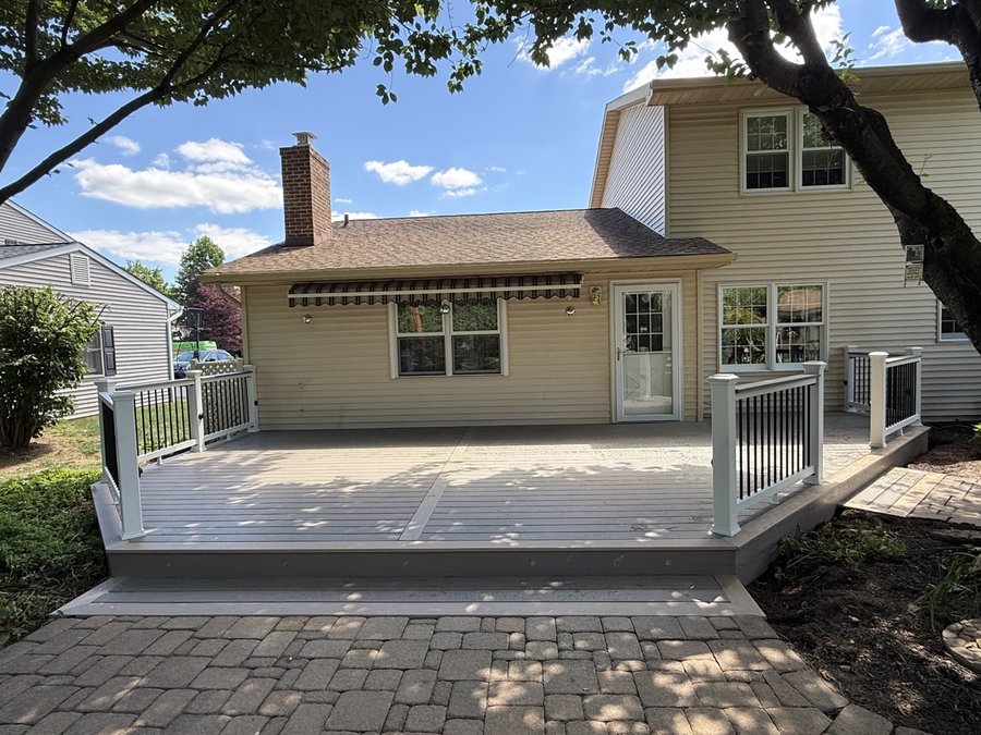 Ground-level composite deck with white and black railings and a paver patio, built by E.B.R Deck Builder