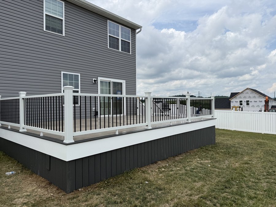 Raised composite deck with white railing, black balusters and dark skirting on a gray house