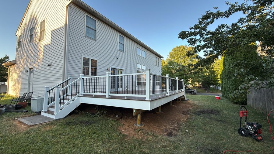 Elevated composite deck with all-white railing and staircase in a green backyard