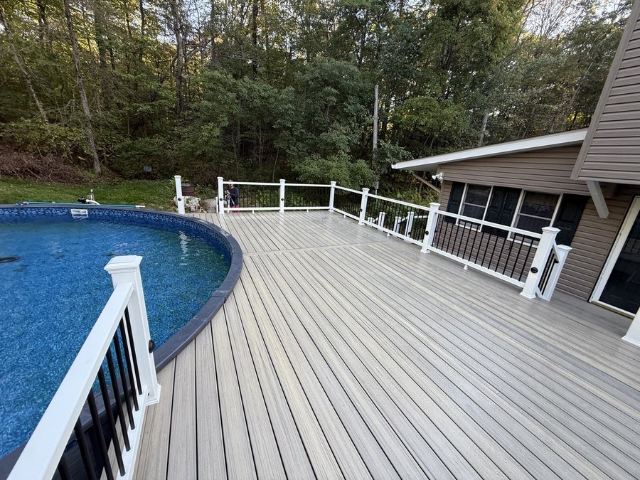 Large light-gray composite pool deck wrapping around an oval pool, with white railing